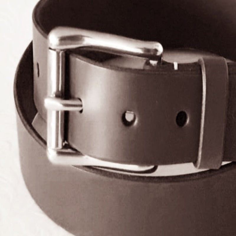 A close up of a brown leather belt with a stainless steel wave roller heel bar belt buckle on a white background. An example of what the stainless steel belt buckle will look like in use. This purchase does not include the belt.