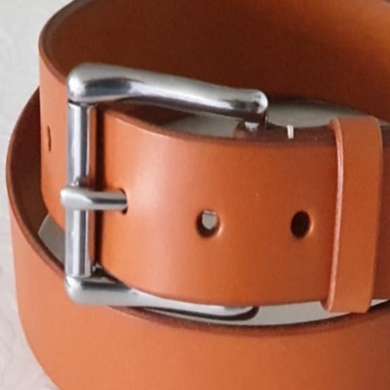 A close up of a tan leather belt with a stainless steel wave roller heel bar belt buckle on a white background. An example of what the stainless steel belt buckle will look like in use. This purchase does not include the belt.